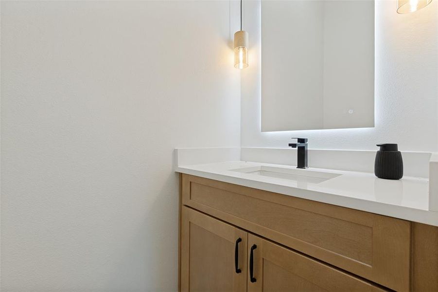 Bathroom vanity featuring a light wood-finish cabinet with matte black hardware, a white countertop, an undermount sink, and a black single-lever faucet