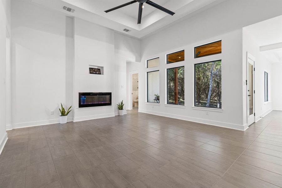 Unfurnished living room featuring a towering ceiling, a glass covered fireplace, a raised ceiling, and a ceiling fan