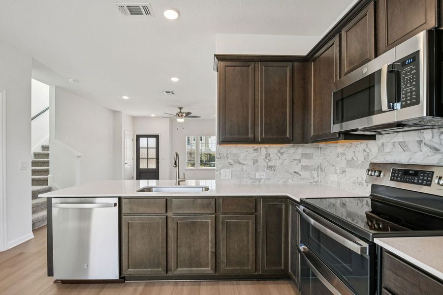 Kitchen with dark brown cabinetry, appliances with stainless steel finishes, a peninsula, recessed lighting, and decorative backsplash