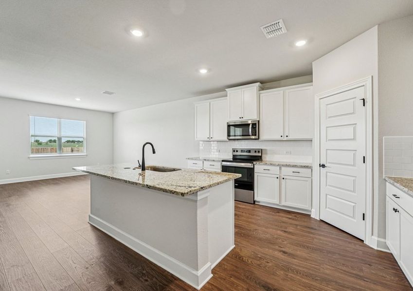 Kitchen featuring a granite island, white cabinetry, and stainless steel appliances with wood-look vinyl flooring. Kitchen featuring a granite island, white cabinetry, and stainless steel appliances with wood-look vinyl flooring.
