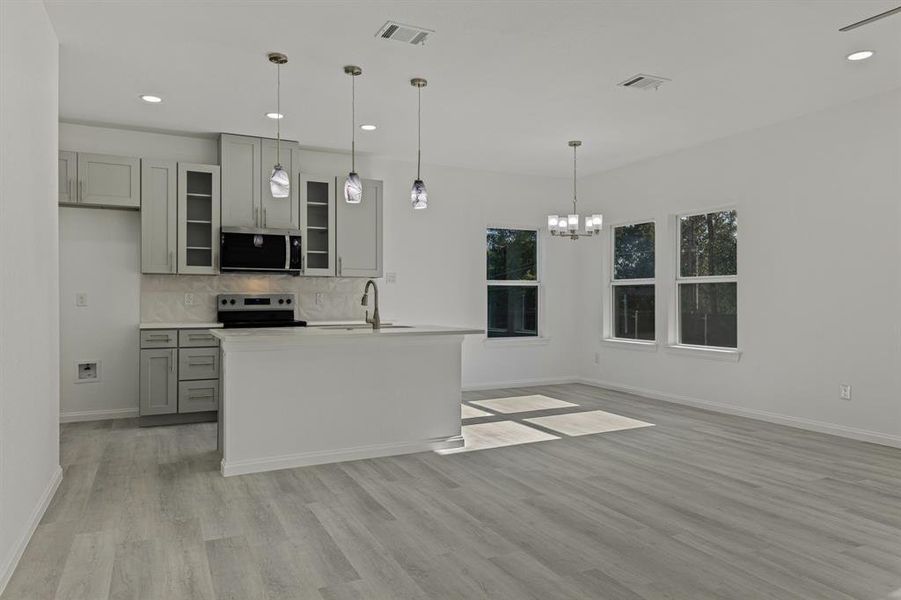 Kitchen with gray cabinetry, glass insert cabinets, recessed lighting, hanging light fixtures, and stainless steel appliances