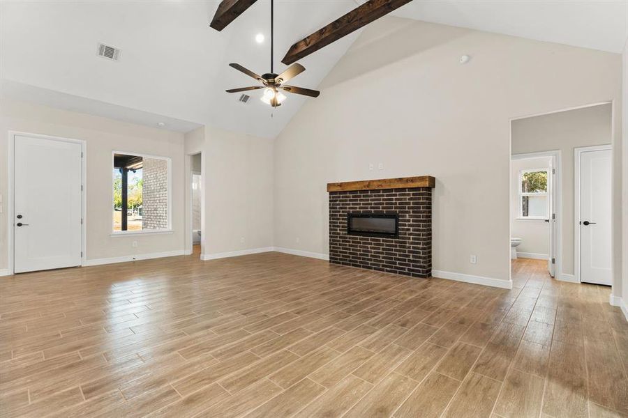 Unfurnished living room with high vaulted ceiling, a glass covered fireplace, light wood-style flooring, beamed ceiling, and recessed lighting