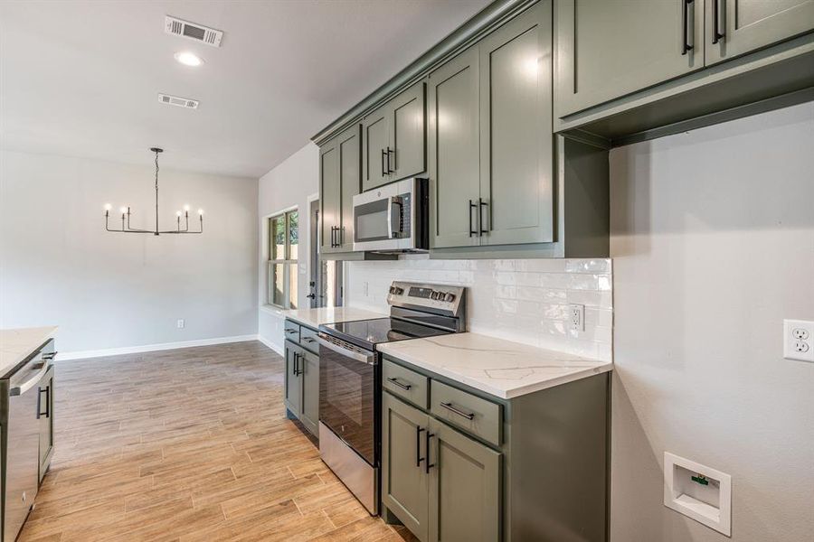 Kitchen with light stone counters, tasteful backsplash, a chandelier, appliances with stainless steel finishes, and light wood-type flooring