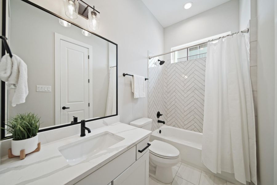The third bathroom features ceramic tile floors, a quartz vanity with black hardware and a tub/shower combo framed by herringbone-patterned subway tile. A black-framed mirror and sleek overhead light complete the look of the bathroom. The third bathroom features ceramic tile floors, a quartz vanity with black hardware and a tub/shower combo framed by herringbone-patterned subway tile. A black-framed mirror and sleek overhead light complete the look of the bathroom.