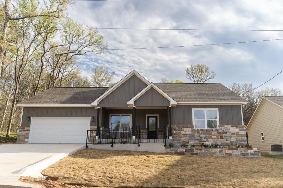 View of front of property with board and batten siding, a porch, concrete driveway, a garage, and stone siding