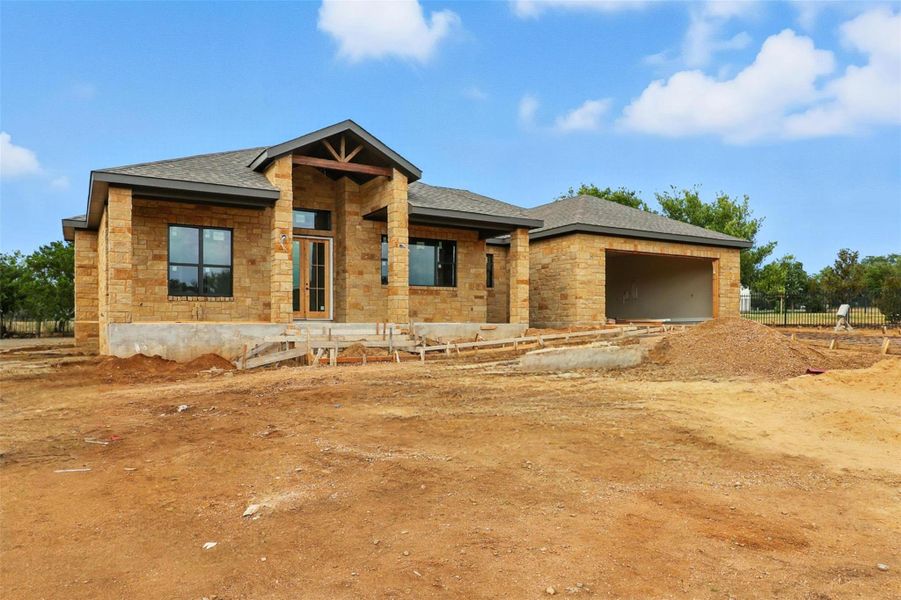 View of front facade with stone siding, an attached garage, roof with shingles, and a patio View of front facade with stone siding, an attached garage, roof with shingles, and a patio