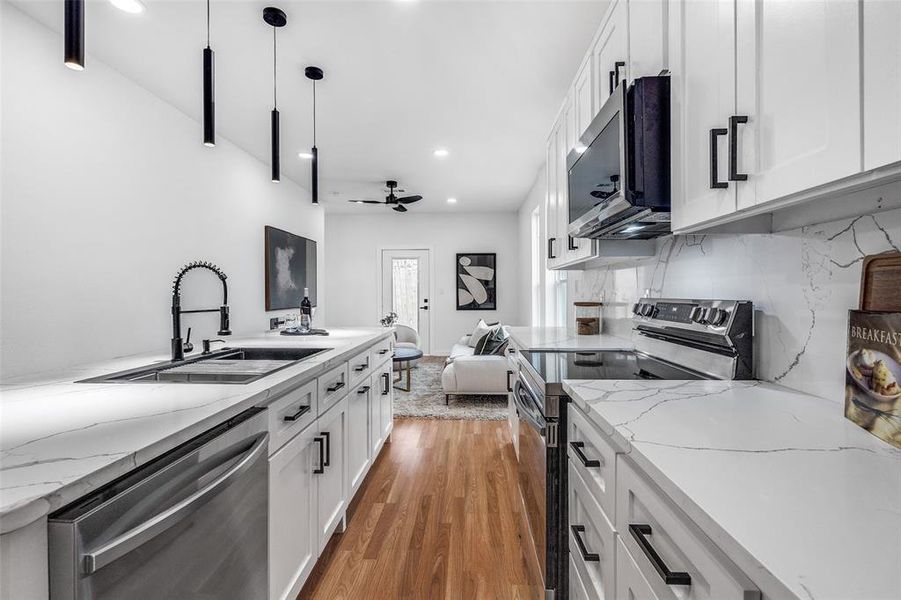 Kitchen with appliances with stainless steel finishes, dark wood-type flooring, white cabinets, light stone counters, and recessed lighting Kitchen with appliances with stainless steel finishes, dark wood-type flooring, white cabinets, light stone counters, and recessed lighting