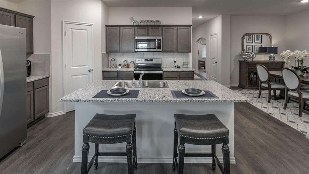 Kitchen with a breakfast bar, stainless steel appliances, recessed lighting, dark wood-type flooring, and an island with sink