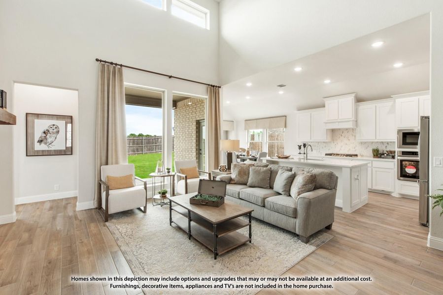 Open-concept living room with high ceilings and hardwood floors, open to white kitchen with island and backyard view