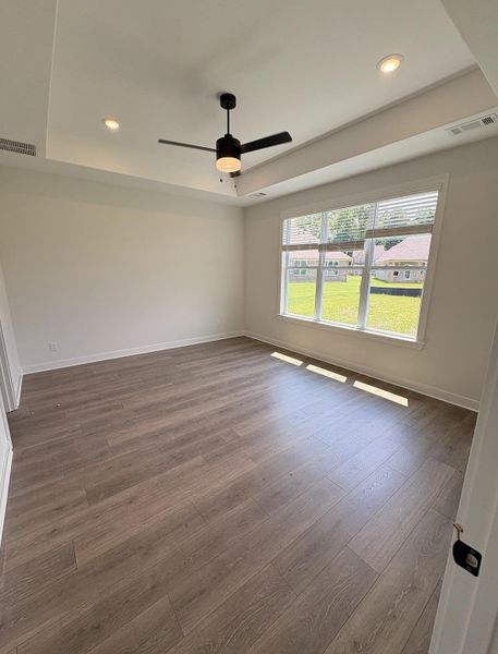 Spacious room featuring wood-finish flooring, a tray ceiling with recessed lighting, and a modern ceiling fan Spacious room featuring wood-finish flooring, a tray ceiling with recessed lighting, and a modern ceiling fan