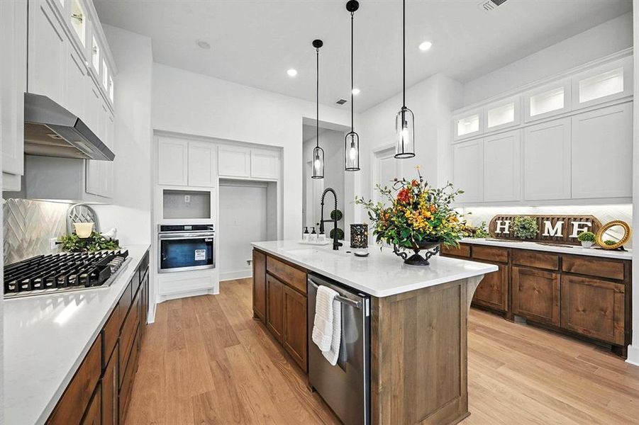 Kitchen with glass insert cabinets, a center island with sink, tasteful backsplash, light wood-style flooring, and hanging light fixtures