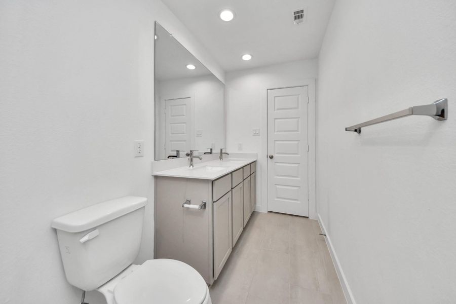 Secondary bath features tile flooring, bath/shower combo with tile surround, light stained wood cabinets, beautiful light countertop. Sample photo of completed home with similar floor plan. Actual colors and selections may vary.