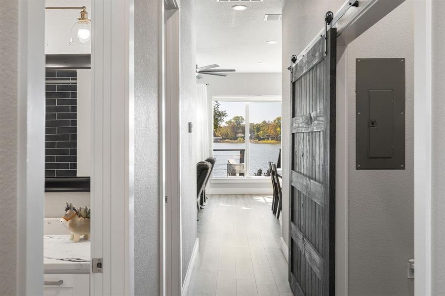 Hall featuring a barn door, a textured wall, electric panel, light wood-style flooring, and a water view