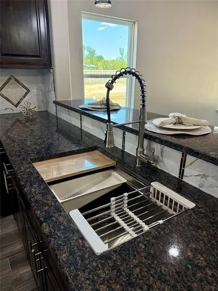 Gleaming dark granite countertops featuring an undermount stainless steel sink with an integrated drying rack and cutting board