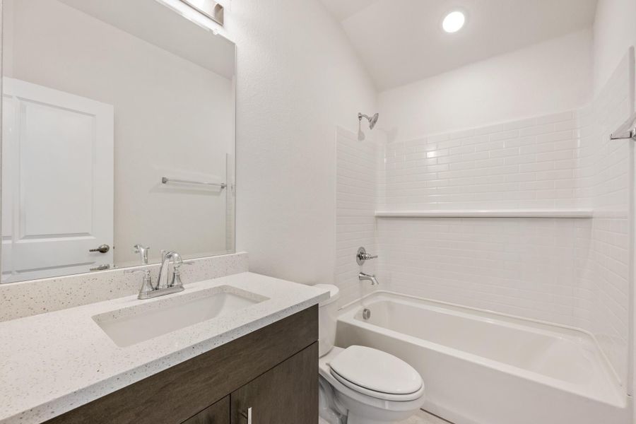 Bathroom with dark wood vanity, quartz countertop, and white tub-shower combo with subway tile surround