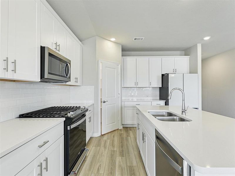 Kitchen featuring appliances with stainless steel finishes, backsplash, sink, light hardwood / wood-style flooring, and white cabinetry