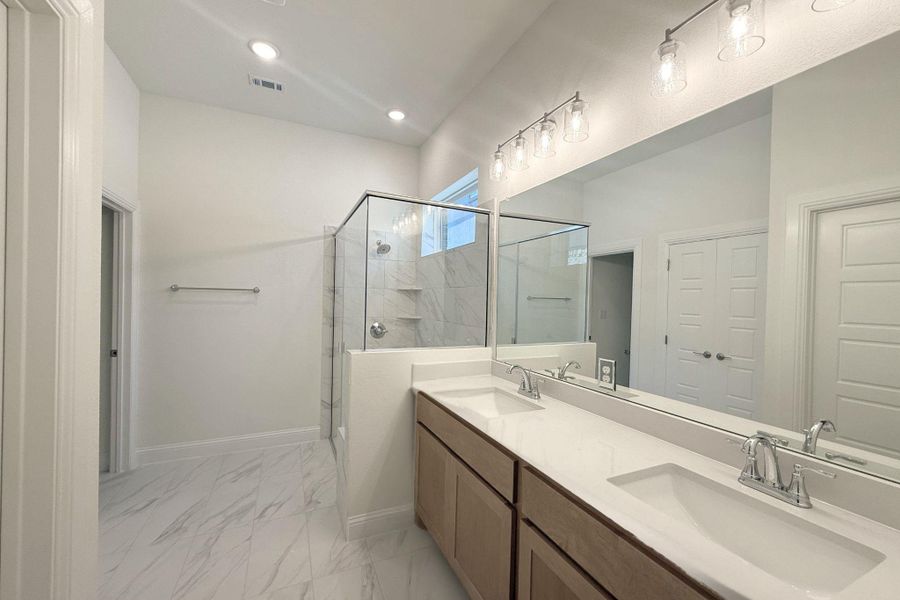 Contemporary bathroom featuring a double vanity with light wood-finish cabinetry, white countertops, and chrome fixtures