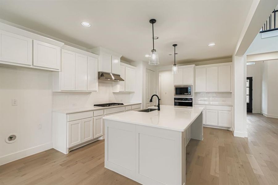Kitchen featuring backsplash, white cabinets, light wood finished floors, hanging light fixtures, and recessed lighting Kitchen featuring backsplash, white cabinets, light wood finished floors, hanging light fixtures, and recessed lighting