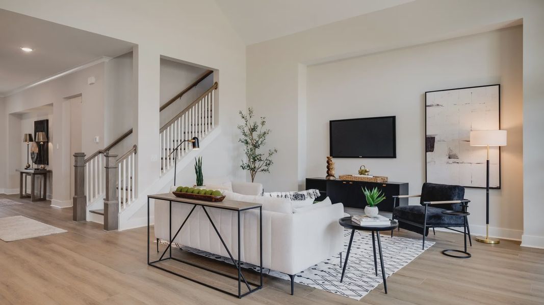 Large living room area with vaulted ceiling next to staircase and kitchen