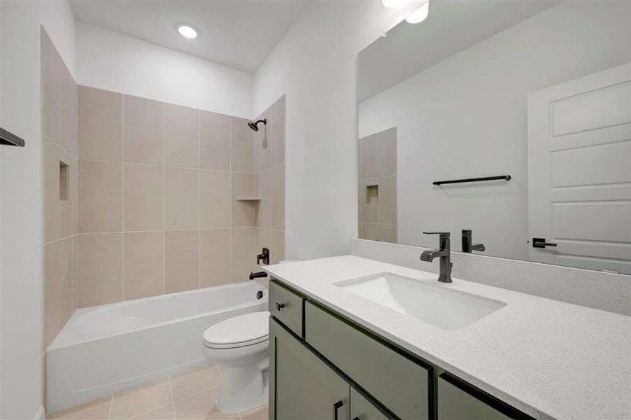 Bathroom featuring a built-in tub with tile surround, a single vanity with a quartz countertop, an integrated sink, and matte black fixtures Bathroom featuring a built-in tub with tile surround, a single vanity with a quartz countertop, an integrated sink, and matte black fixtures