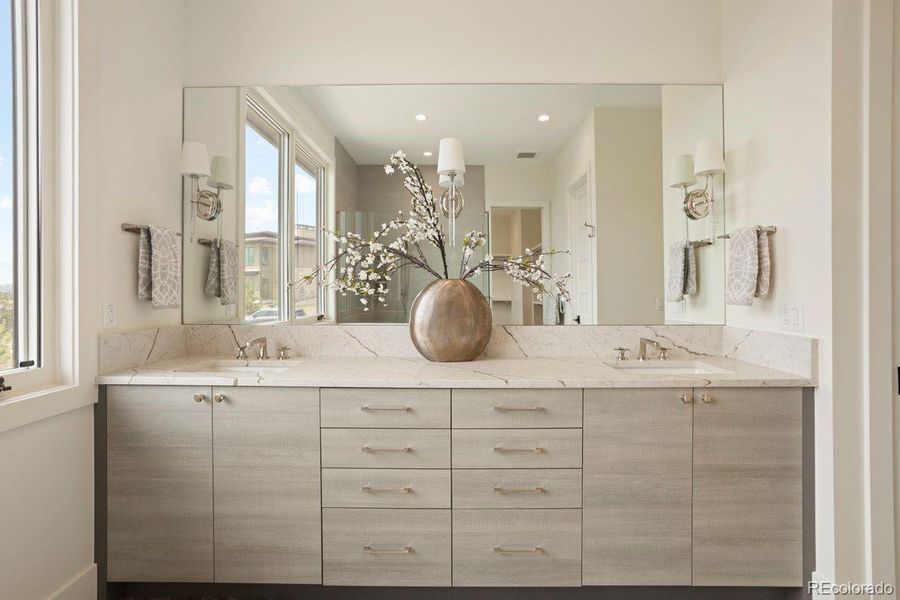 Primary bath with elegant dual-sink vanity with sleek cabinetry, quartz countertops, and a full-width mirror accented by contemporary sconces.