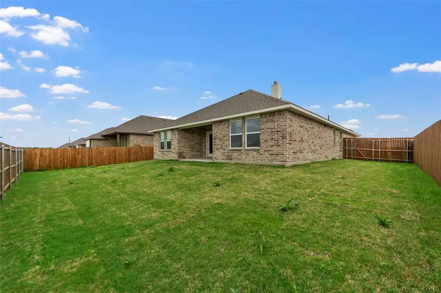 Expansive backyard featuring a brick exterior, shingled roof, a chimney, multiple windows, and wooden privacy fencing