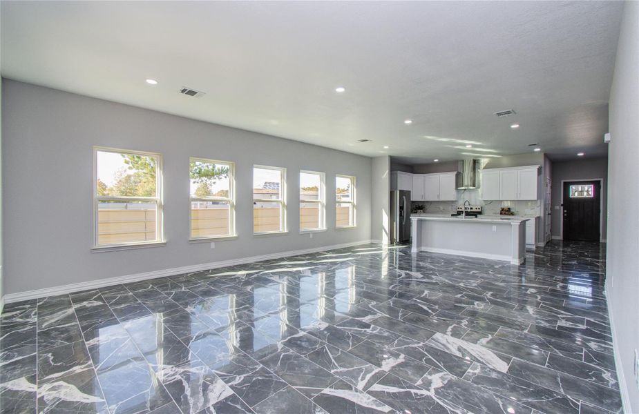 This photo showcases a spacious, open-concept living area with glossy marble floors, recessed lighting, and large windows for natural light. The modern kitchen features sleek white cabinets, stainless steel appliances, and an island, creating a bright and inviting space.