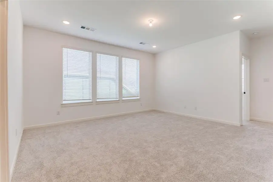 Spacious room featuring light-colored carpeting, three windows with blinds, recessed lighting, and a neutral wall palette