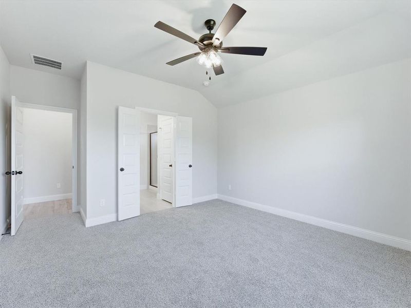 Spacious Primary Suite featuring vaulted ceilings, soft gray carpeting, a contemporary ceiling fan with integrated lighting, and multiple paneled doors with matte black hardware Spacious Primary Suite featuring vaulted ceilings, soft gray carpeting, a contemporary ceiling fan with integrated lighting, and multiple paneled doors with matte black hardware