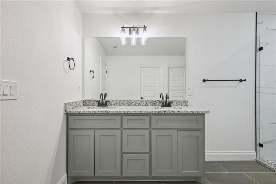 Full bath featuring double vanity, a marble finish shower, and dark tile patterned floors Full bath featuring double vanity, a marble finish shower, and dark tile patterned floors