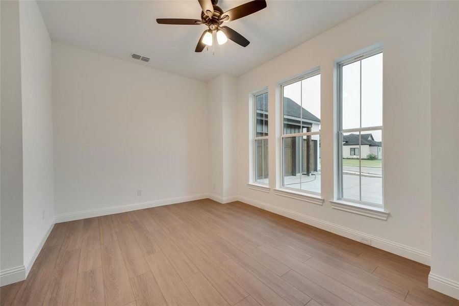 Empty room with light wood-style floors, plenty of natural light, visible vents, and baseboards