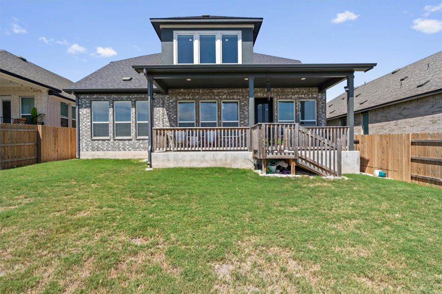 An elevated wooden deck looks out over a grassy yard enclosed by wooden fencing.