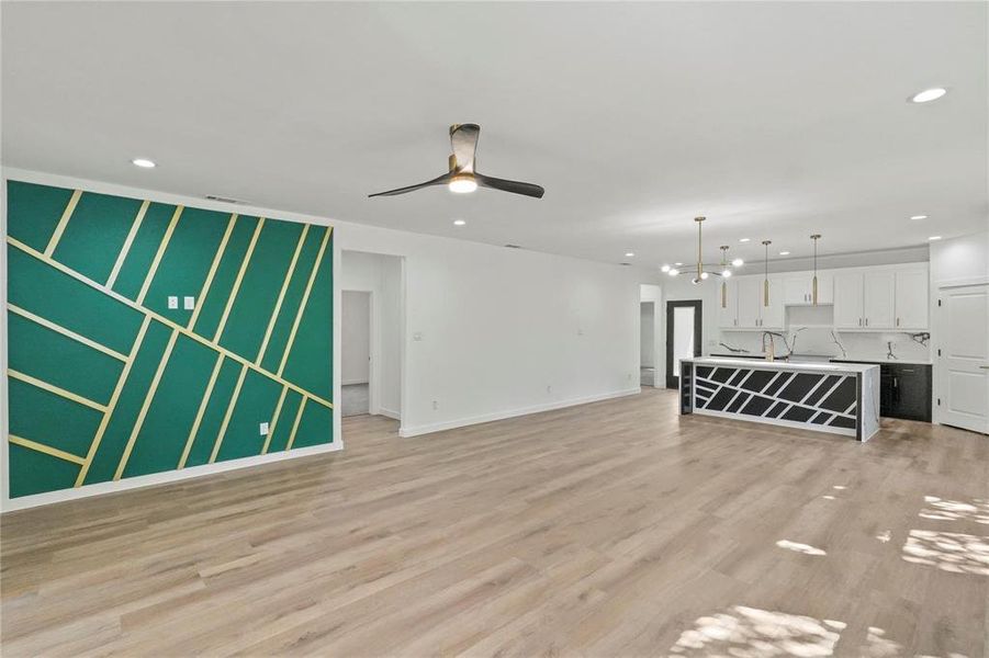 Unfurnished living room with light hardwood / wood-style flooring, ceiling fan with notable chandelier, and sink