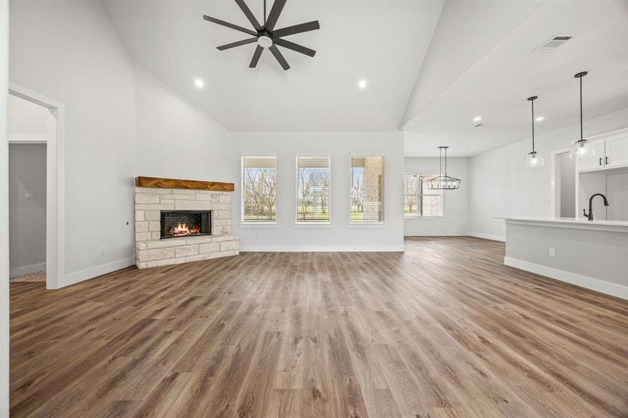 Unfurnished living room featuring a stone fireplace, high vaulted ceiling, light wood-style floors, ceiling fan, and recessed lighting Unfurnished living room featuring a stone fireplace, high vaulted ceiling, light wood-style floors, ceiling fan, and recessed lighting