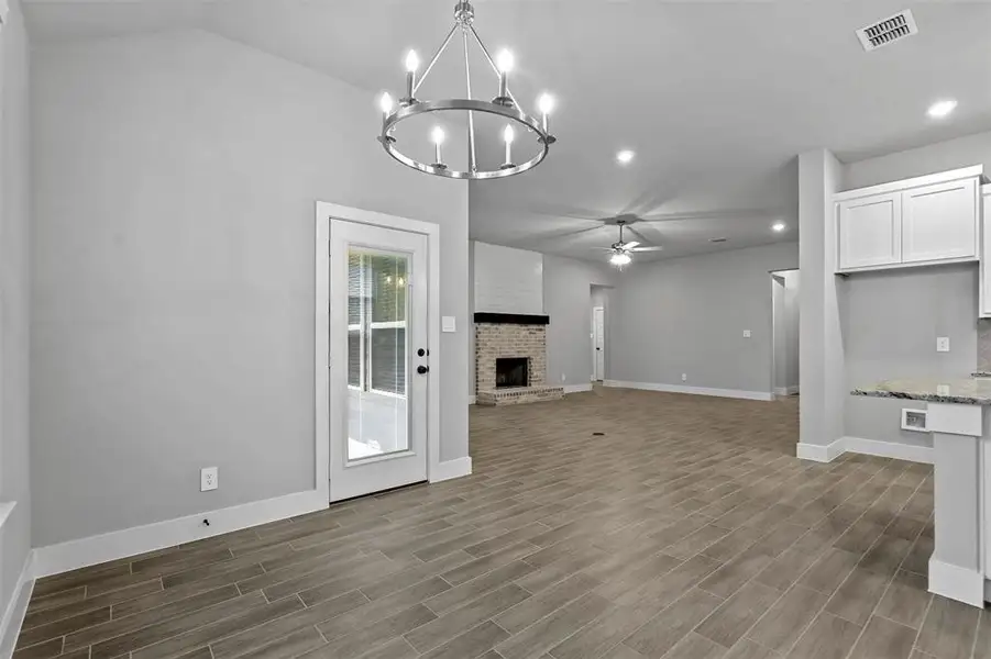 Unfurnished living room with dark hardwood / wood-style flooring, ceiling fan with notable chandelier, vaulted ceiling, and a fireplace