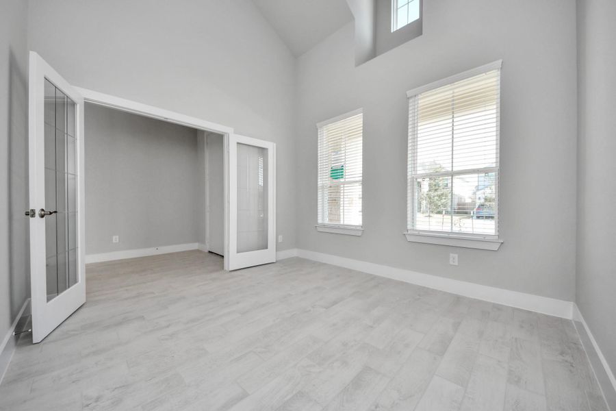 Experience the perfect blend of sophistication and warmth in this home office, boasting elegant wood-look tile flooring and flooded with natural light from expansive windows and French doors.
