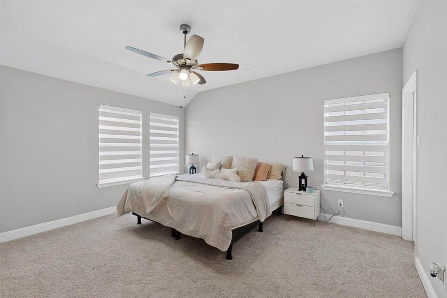 This bedroom features a ceiling fan, carpeted flooring, and windows with horizontal blinds