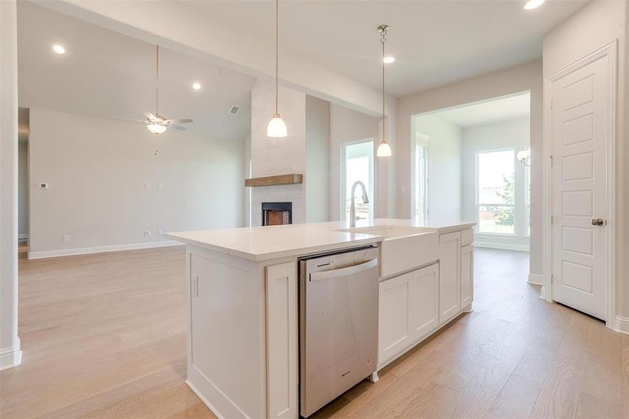 Kitchen featuring a large fireplace, light hardwood / wood-style flooring, ceiling fan, dishwasher, and white cabinetry