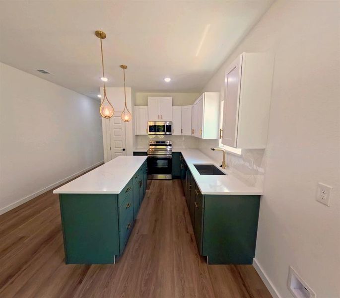 Kitchen featuring white cabinets, green cabinets, appliances with stainless steel finishes, dark wood-style floors, and hanging light fixtures Kitchen featuring white cabinets, green cabinets, appliances with stainless steel finishes, dark wood-style floors, and hanging light fixtures
