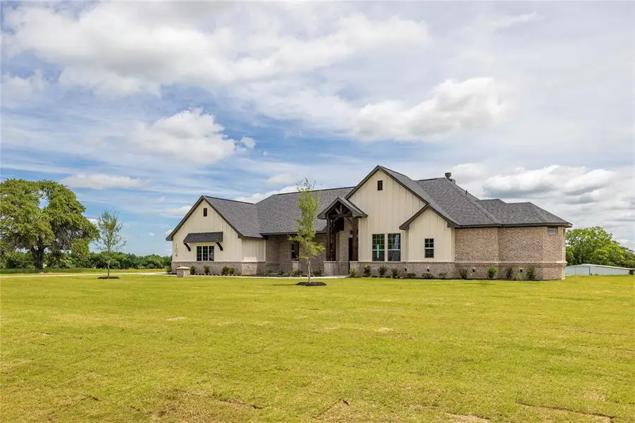 Modern farmhouse style home with a front yard, roof with shingles, and board and batten siding Modern farmhouse style home with a front yard, roof with shingles, and board and batten siding