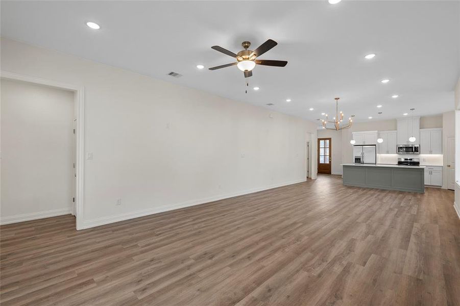Unfurnished living room featuring recessed lighting, dark wood-style flooring, a chandelier, and a ceiling fan Unfurnished living room featuring recessed lighting, dark wood-style flooring, a chandelier, and a ceiling fan