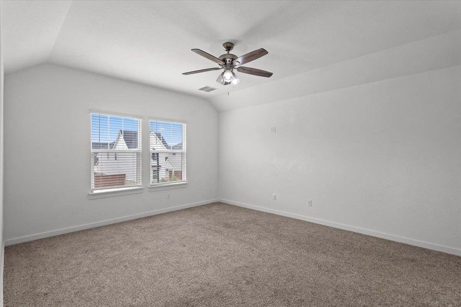A spacious bedroom featuring a vaulted ceiling and ample natural light from two large windows.