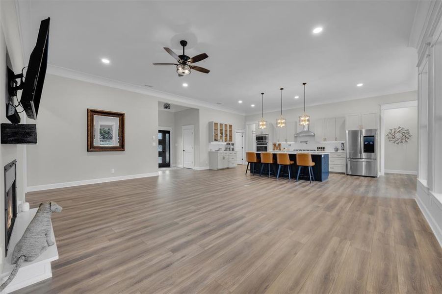 Unfurnished living room with ceiling fan, light hardwood / wood-style floors, and ornamental molding