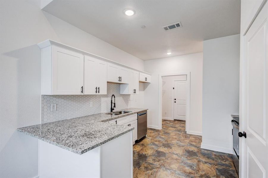 Kitchen featuring white cabinetry, tasteful backsplash, stainless steel dishwasher, tile patterned floors, and sink