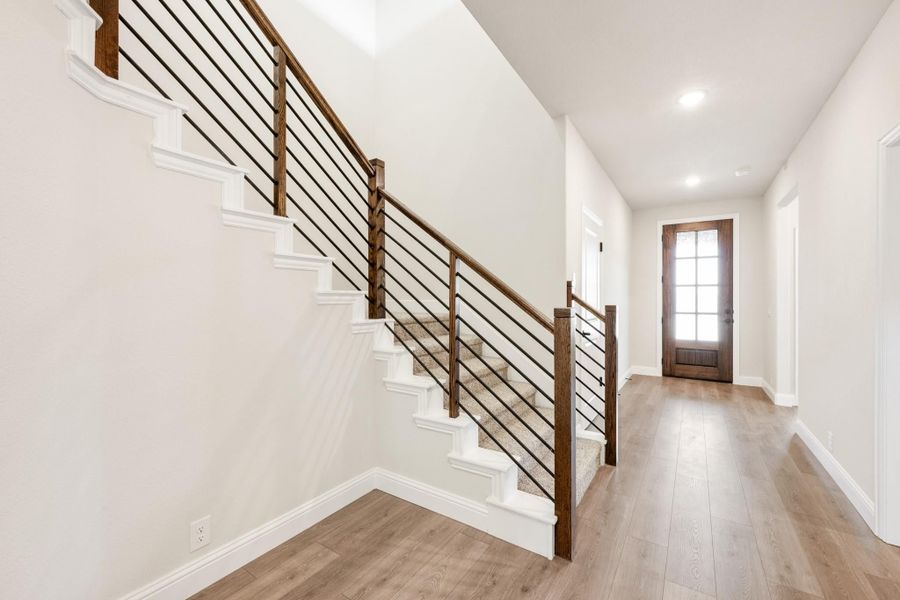 Entryway hallway with staircase featuring wood and metal railing, light hardwood floors, and glass-panel front door Entryway hallway with staircase featuring wood and metal railing, light hardwood floors, and glass-panel front door