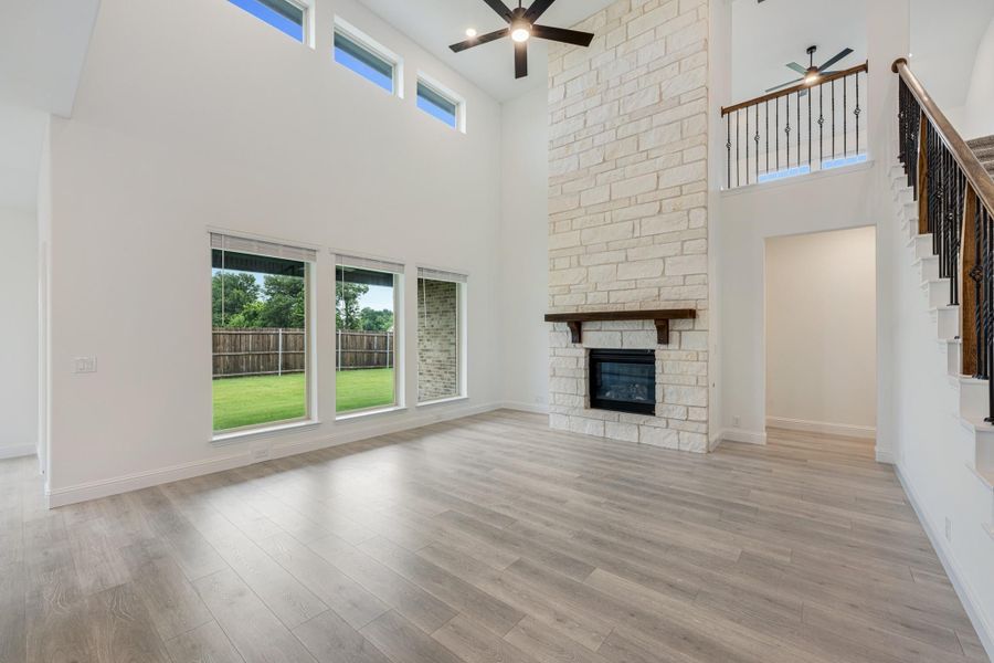 Open living room with two-story stone fireplace, hardwood floors, ceiling fan, and staircase with iron balusters
