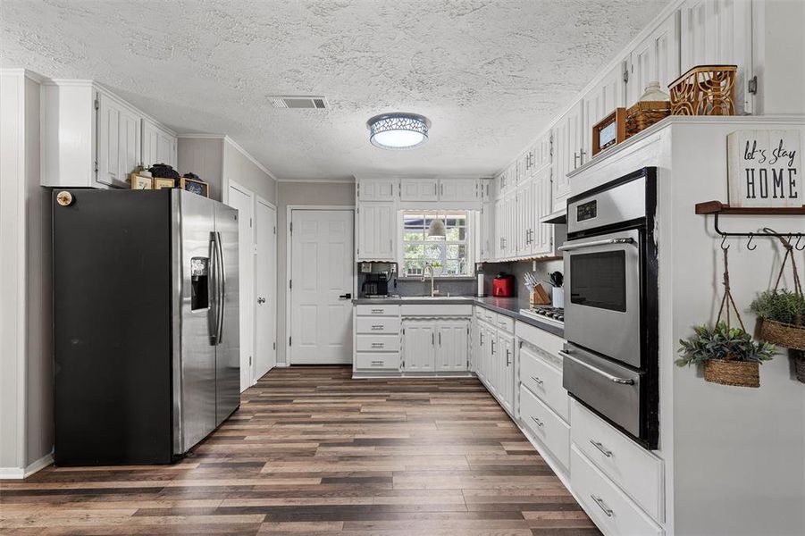 Kitchen featuring stainless steel appliances, a warming drawer, dark wood finished floors, dark countertops, and a textured ceiling Kitchen featuring stainless steel appliances, a warming drawer, dark wood finished floors, dark countertops, and a textured ceiling