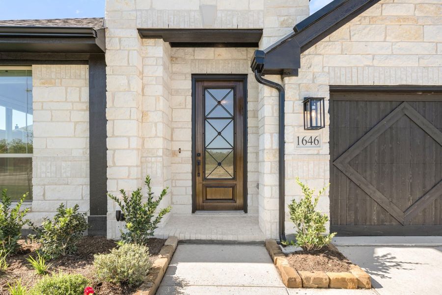 Home entrance with stone exterior, wood and glass front door, and address number 1646 beside garage