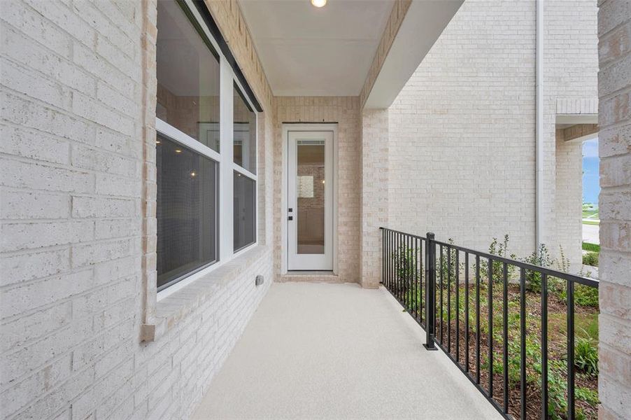 Covered front porch featuring cream brick exterior, white framed windows, and a black wrought iron railing