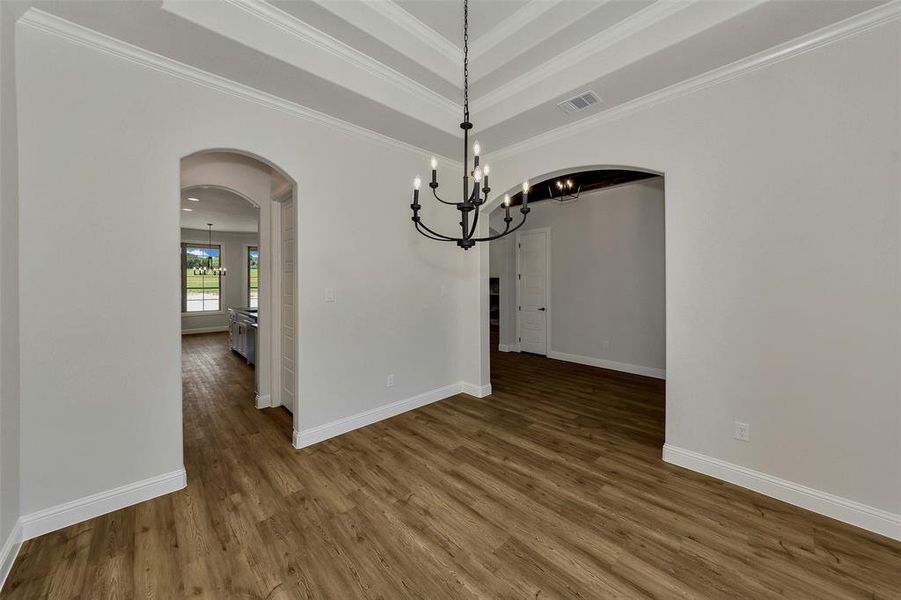 Unfurnished dining area with arched walkways, a chandelier, ornamental molding, wood finished floors, and a tray ceiling